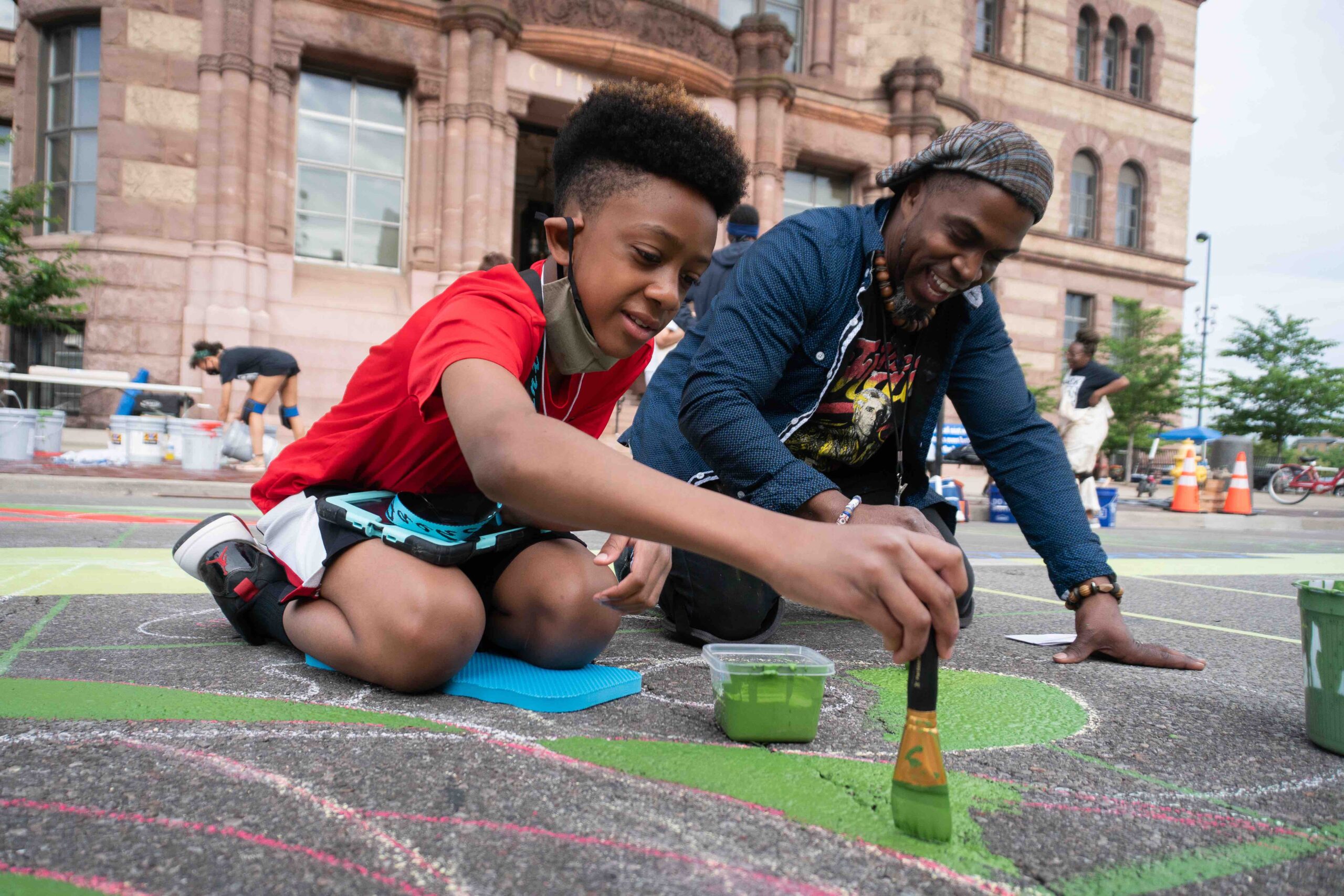 Black father and son painting mural in front of Cincinnati City Hall