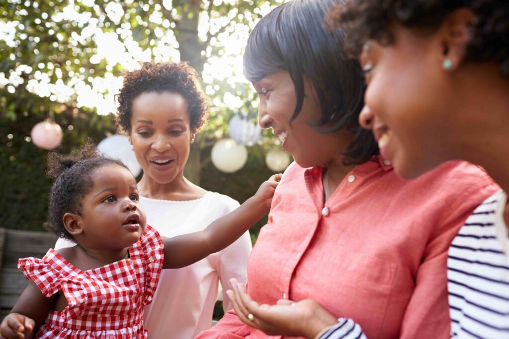 Three Black women smiling at girl toddler