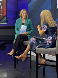 Jill Haubner Miller holding a copy of the book "Infant Mortality and Other Wicked Problems" while talking with Local 12's Liz Bonis